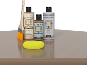 Retique It Barn Wood Kit with Light Wood Wood'n Primer, Barn Wood Gel Stain Alternative, Gloss Polytique It topcoat, paintbrush, and yellow sponge on a tabletop.