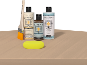 Retique It® Pecan Multipurpose Kit contents with Bleached Wood Liquid Wood primer, Pecan gel stain alternative, Tripletique matte top coat, paintbrush, and yellow sponge displayed on a light wood surface.