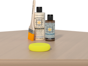Retique It® Pecan Multipurpose Kit contents with Bleached Wood Liquid Wood primer, Pecan gel stain alternative, paintbrush, and yellow sponge displayed on a light wood surface.