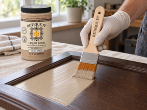 Gloved hand brushing Retique It Light Wood Liquid Wood onto a dark cabinet door, with a 32 oz jar nearby.