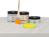 Retique It® White Wash Multipurpose Kit contents with Liquid Wood primer, White Wash gel stain alternative, PolyTique It® matte exterior top coat, paintbrush, and yellow sponge displayed on a white wood surface.