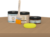 Retique It® Pecan Multipurpose Kit contents with Light Wood Liquid Wood primer, Pecan gel stain alternative, Tripletique matte interior top coat, paintbrush, and yellow sponge displayed on a wood surface.