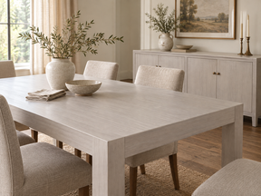Antique White dining table and matching sideboard with cream upholstered chairs in a bright neutral dining room.