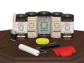 Retique It Java Wood'n Kit featuring Java Liquid Wood stain, Light Wood primer, Java Gel Stain Alternative, paint brush, white roller, yellow sponge, and red graining tools displayed on a dark wood tabletop.
