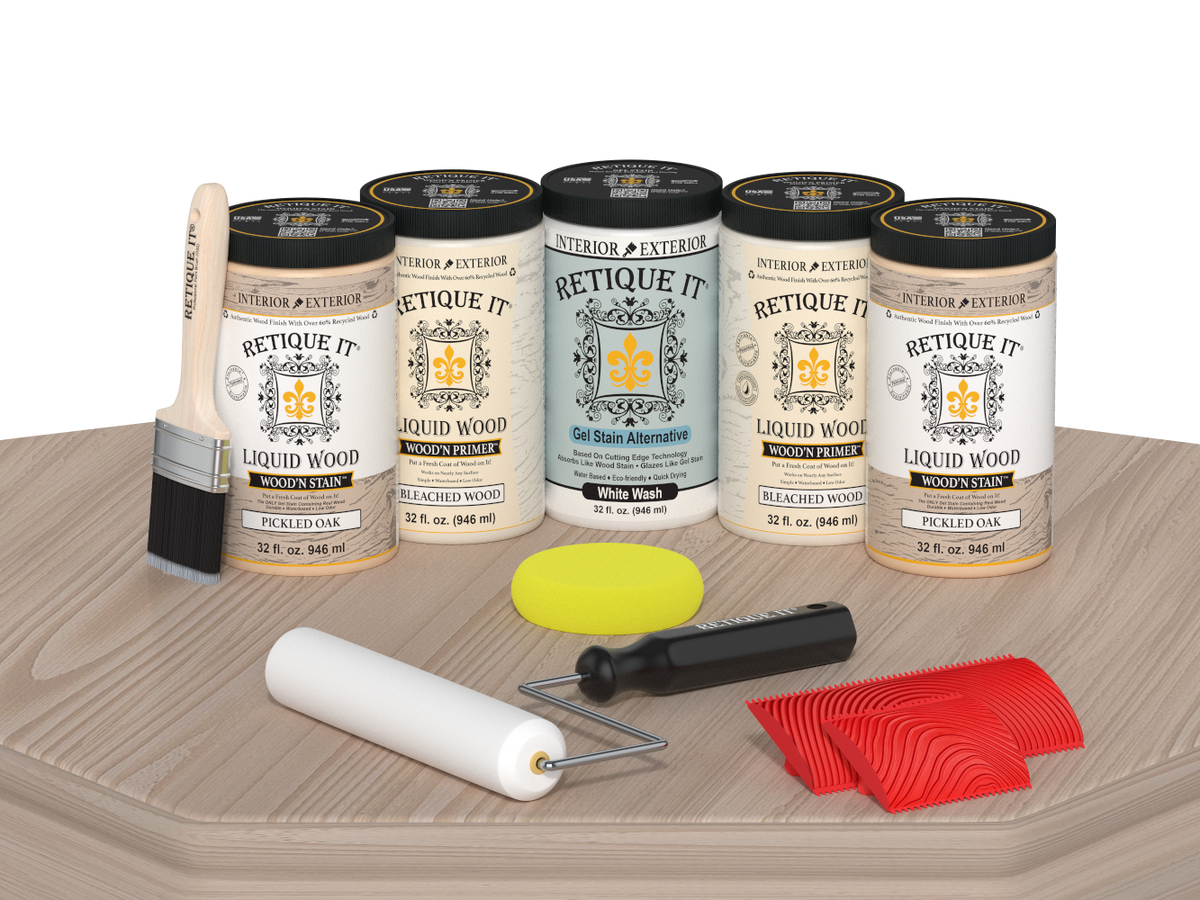 Retique It Sun Bleached finishing system displayed on a light wood surface, featuring Liquid Wood Wood'n Primer in Bleached Wood, Liquid Wood Wood'n Stain in Pickled Oak, White Wash Gel Stain Alternative, paintbrush, roller, yellow sponge, and red graining tools for creating a weathered sun-bleached wood finish.